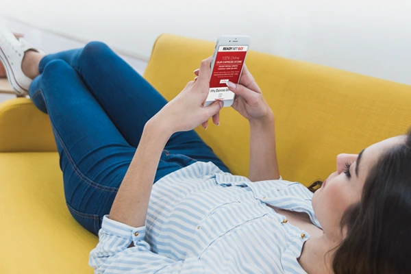 Young woman laying back on couch as she scrolls through her email inbox